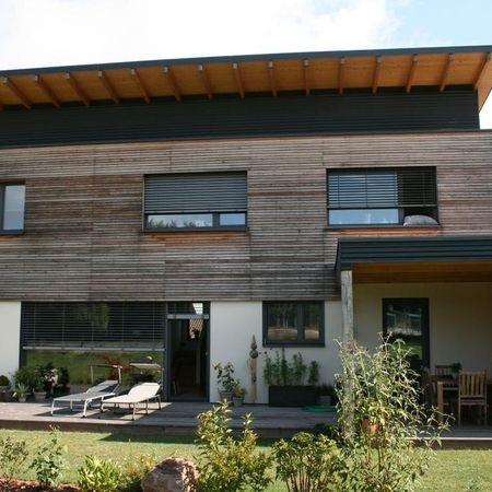 Holzfassade und Anbau mit Sinuswellen